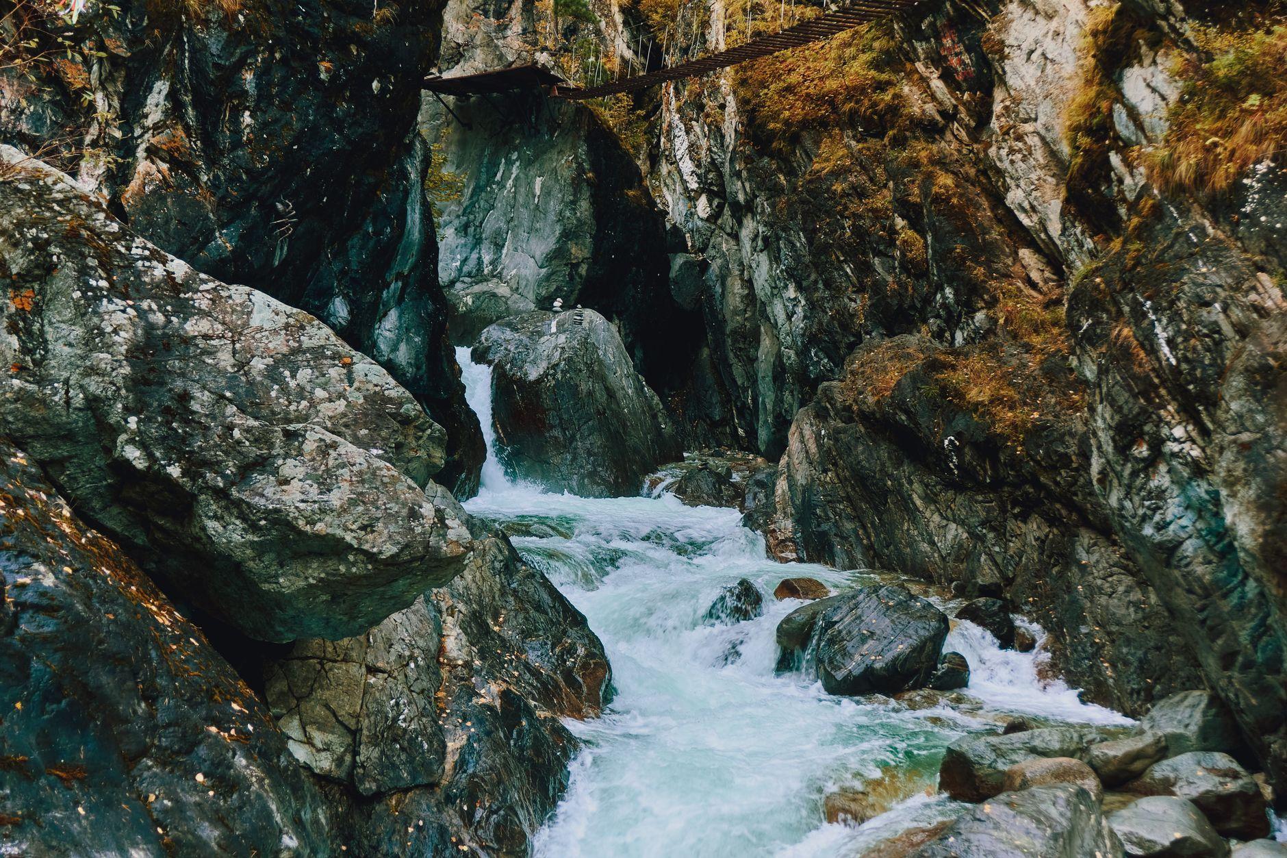 A turquoise mountain stream rushing through a rocky gorge beneath a footbridge