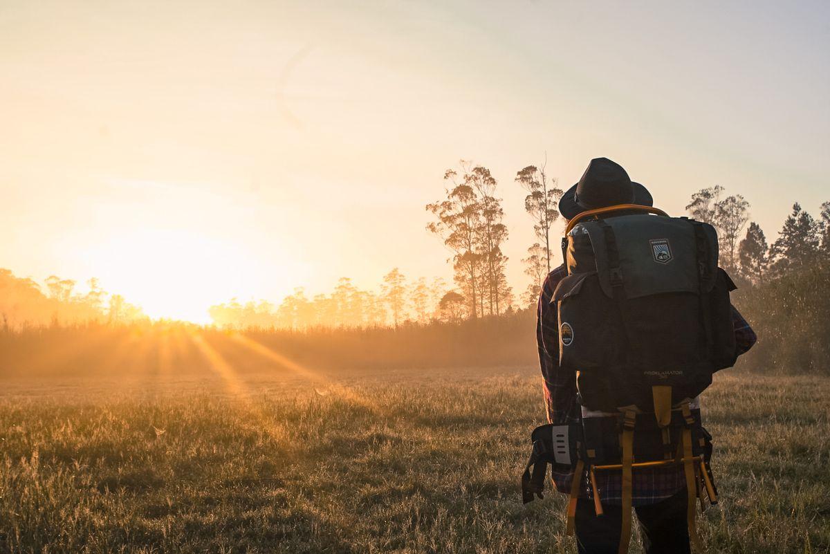 Randonneur avec sac à dos face à un lever de soleil doré sur une lisière brumeuse